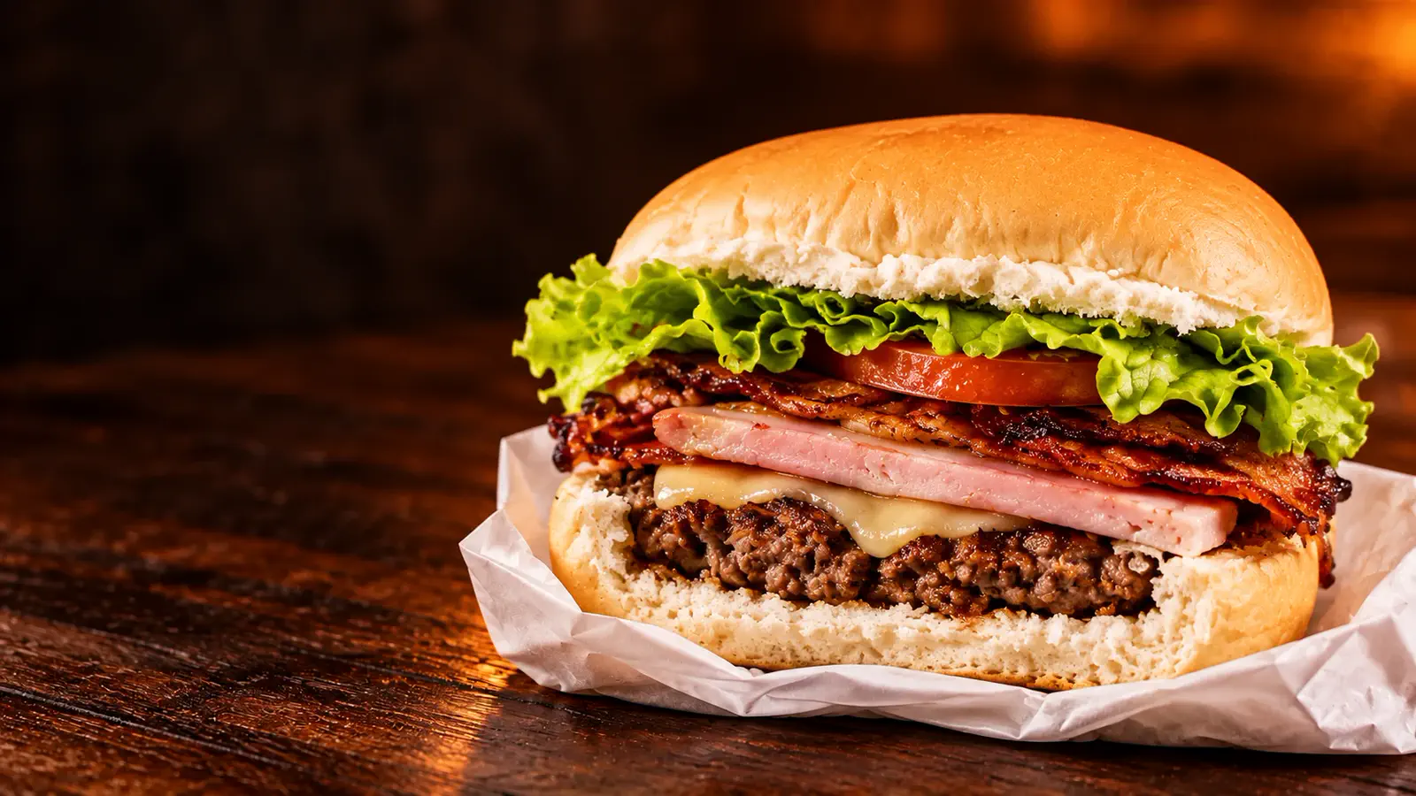 Recriação ilustrativa de um lanche da Léo Burger cortado ao meio, com carne, queijo, presunto, bacon, tomate e alface